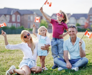A happy family sitting in park holding small Canadian flags in their flags